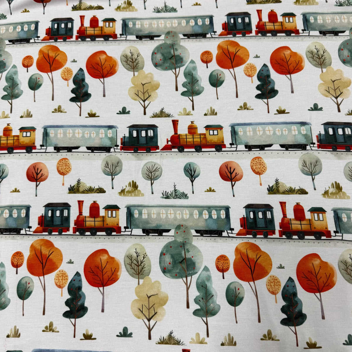 Nature's Fabrics train print fabric with autumn trees, colorful locomotives, and eco-friendly natural cotton design