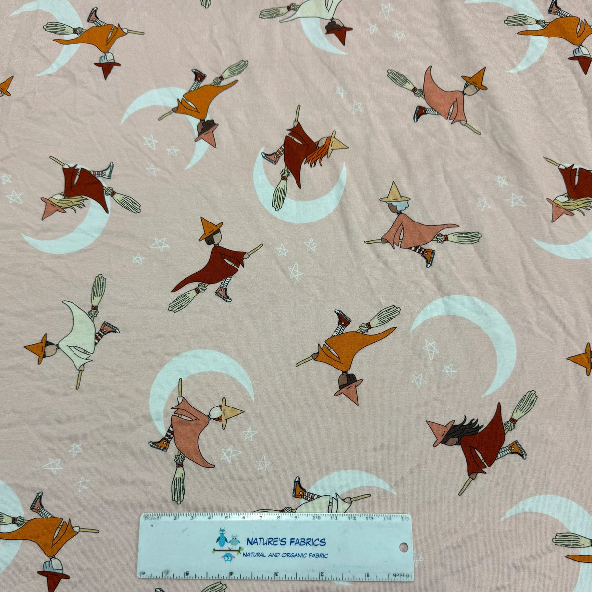Nature's Fabrics witch print organic cotton fabric with flying witches, crescent moons, and stars on a soft pink background