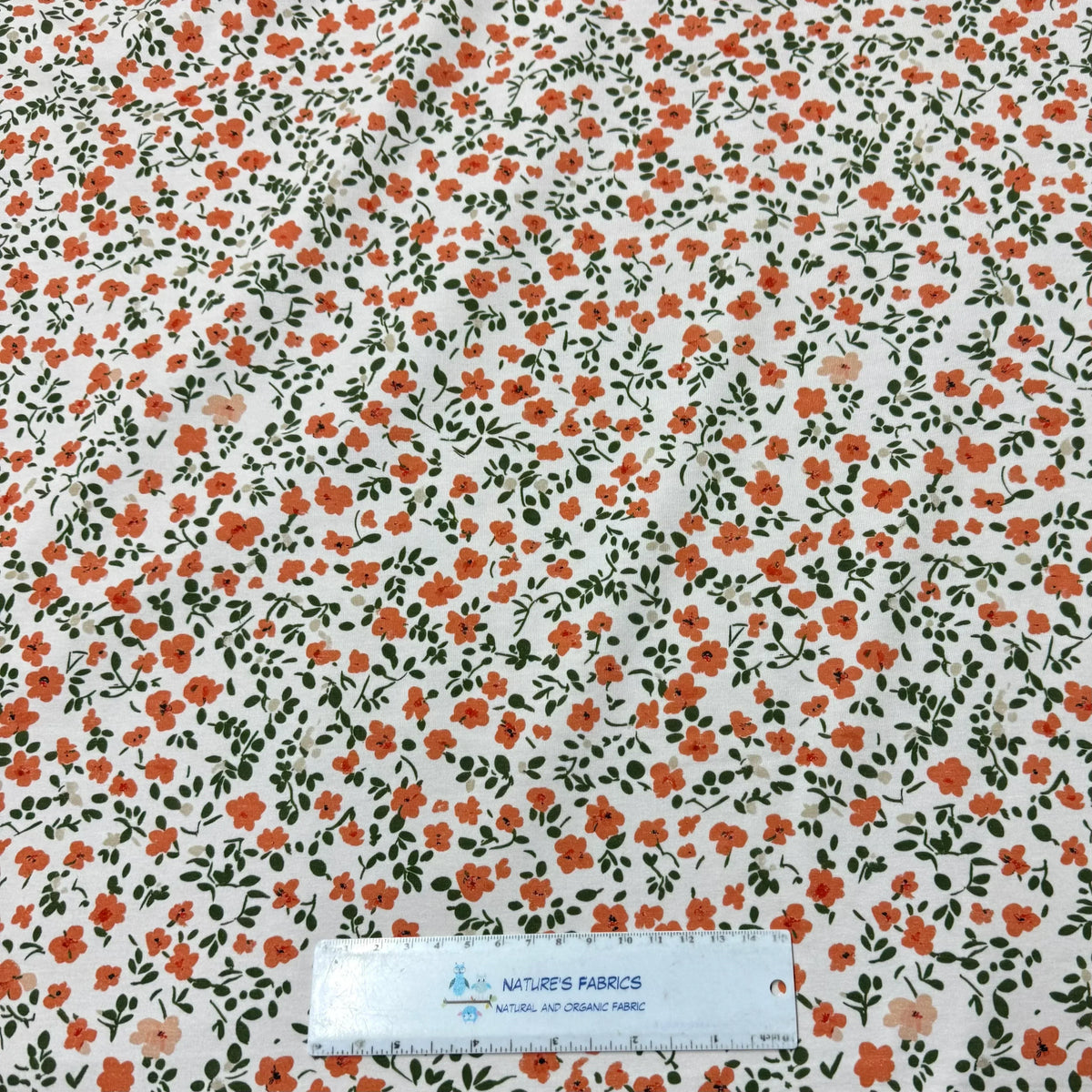 Nature's Fabrics orange floral print on white organic cotton fabric with green leaves, ruler for scale