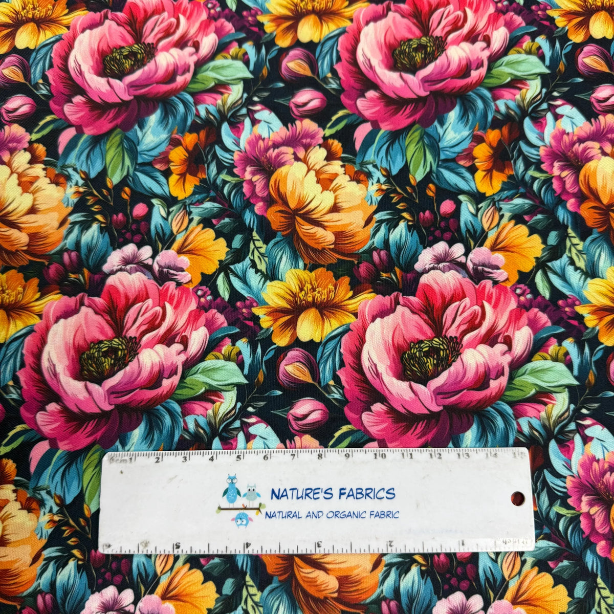Vibrant floral fabric with pink, yellow, and teal blooms on black background, measured by Nature's Fabrics ruler