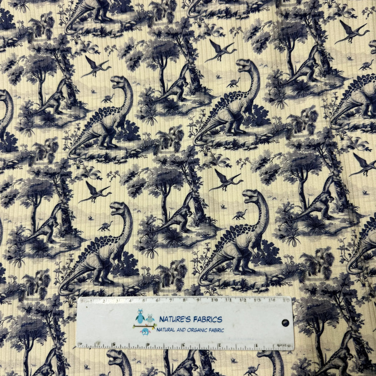 Nature's Fabrics dinosaur toile print fabric with blue prehistoric scene on cream background, ruler for scale
