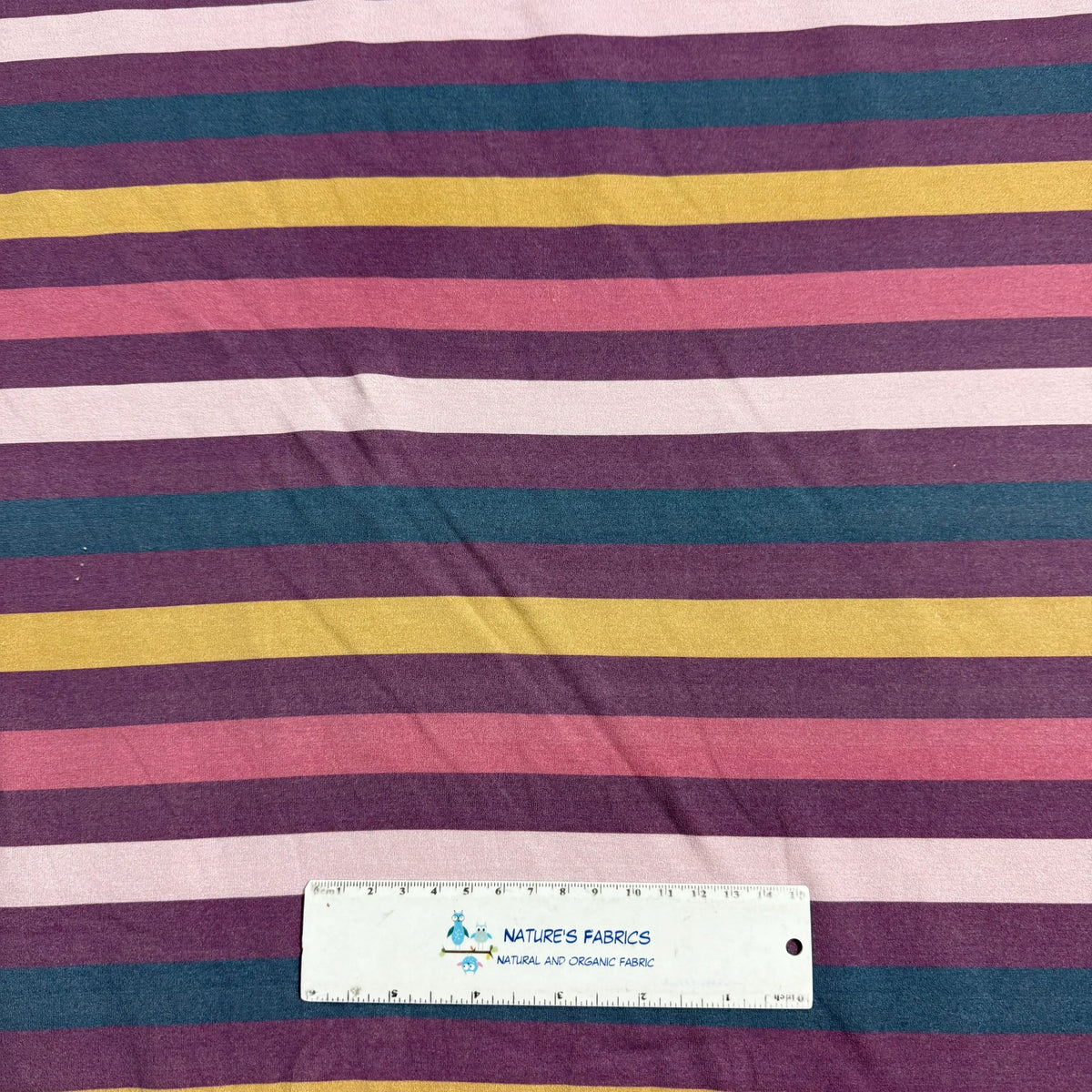 Nature's Fabrics multi-color striped organic cotton fabric with ruler for scale, featuring purple, teal, yellow, pink, and white stripes.