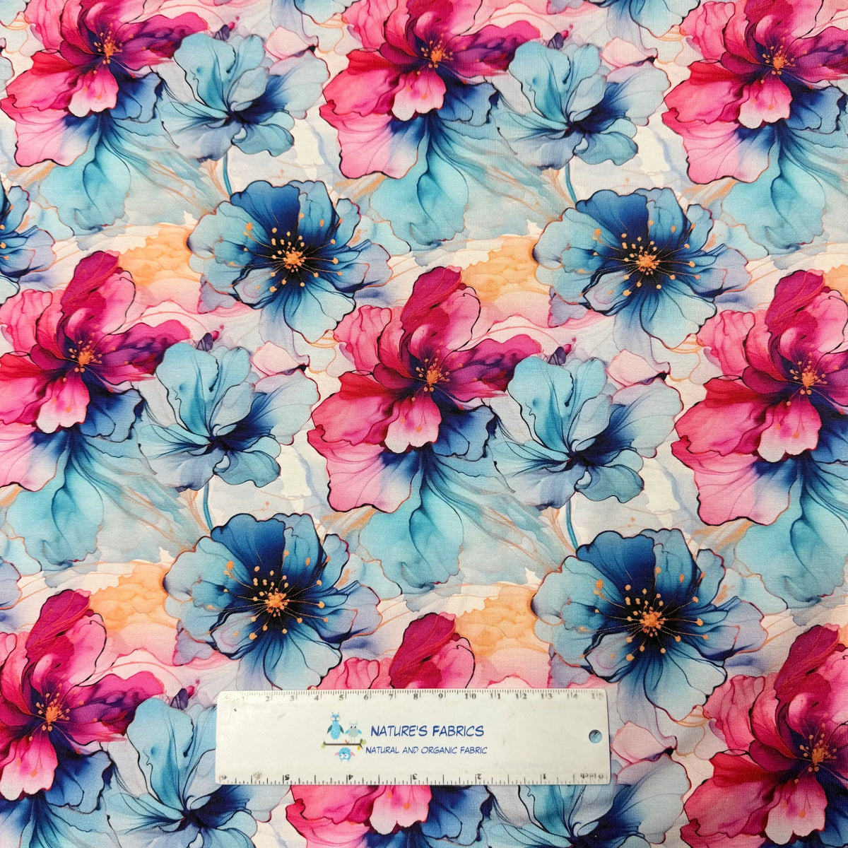 Vibrant pink and blue floral print fabric by Nature's Fabrics, featuring watercolor-style hibiscus blooms on natural organic cotton.