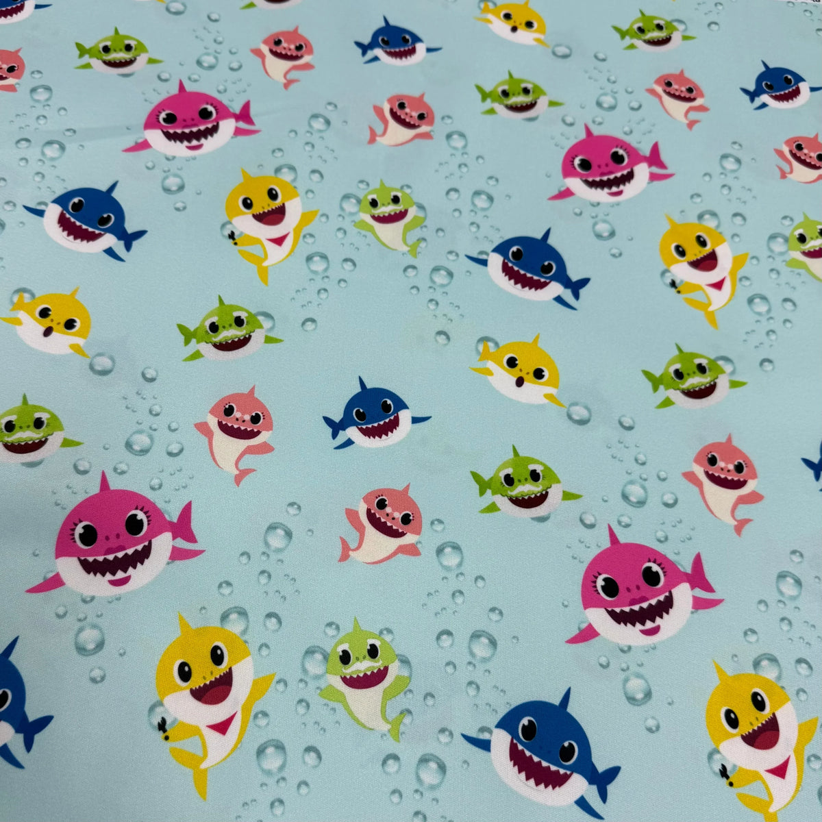 Colorful baby shark print fabric by Nature's Fabrics, featuring playful sharks and bubbles on a light blue background.