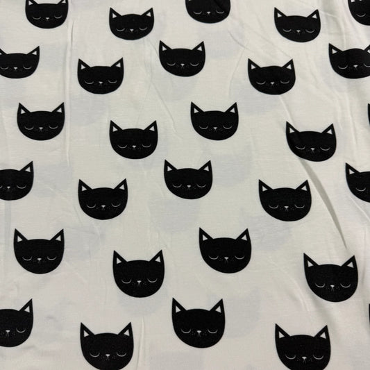 Nature's Fabrics white cotton fabric featuring a repeating black cat face pattern.