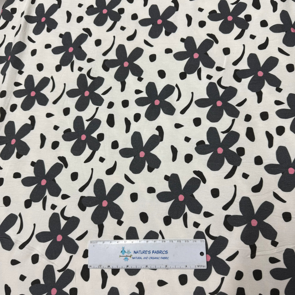 Nature's Fabrics black floral print on cream organic cotton fabric with pink centers, shown with ruler for scale