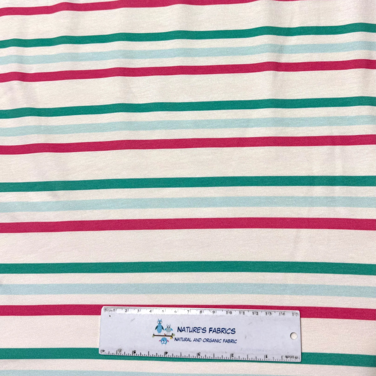 Nature's Fabrics organic cotton stripe fabric in pink, green, blue on white, with ruler for scale