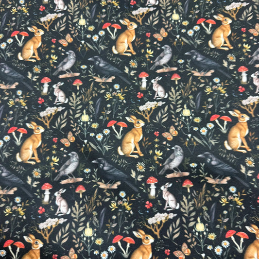 Nature's Fabrics black fabric with a woodland pattern of hares, crows, and red mushrooms.