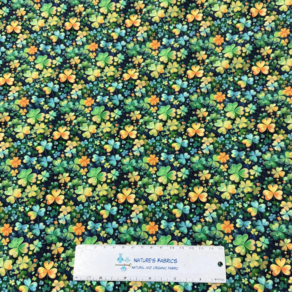 Nature's Fabrics shamrock print fabric with green, orange, and blue clovers on dark background, organic cotton by the yard