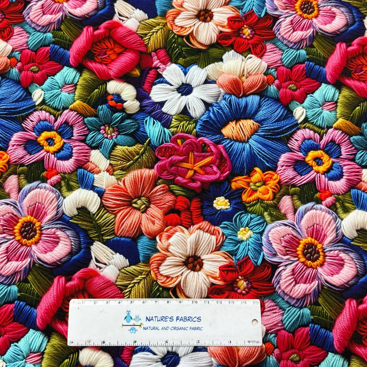 Vibrant floral embroidery fabric by Nature's Fabrics, featuring colorful 3D flowers on natural organic cotton, perfect for sewing projects.
