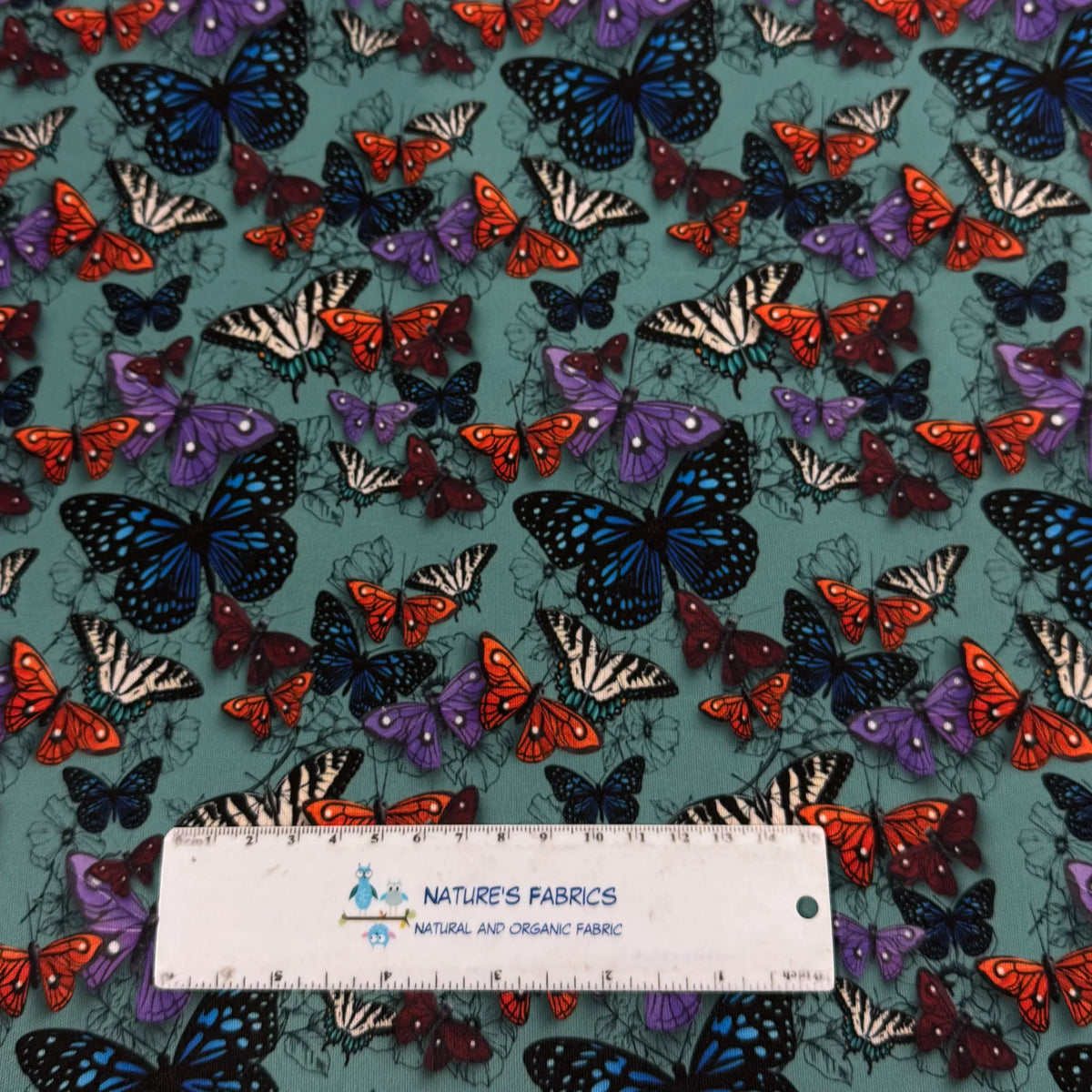 Nature's Fabrics butterfly print organic cotton fabric with vibrant blue, orange, and purple butterflies on teal background
