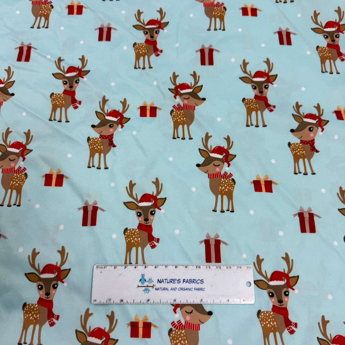 Nature's Fabrics festive reindeer print fabric with Santa hats and gifts on light blue background