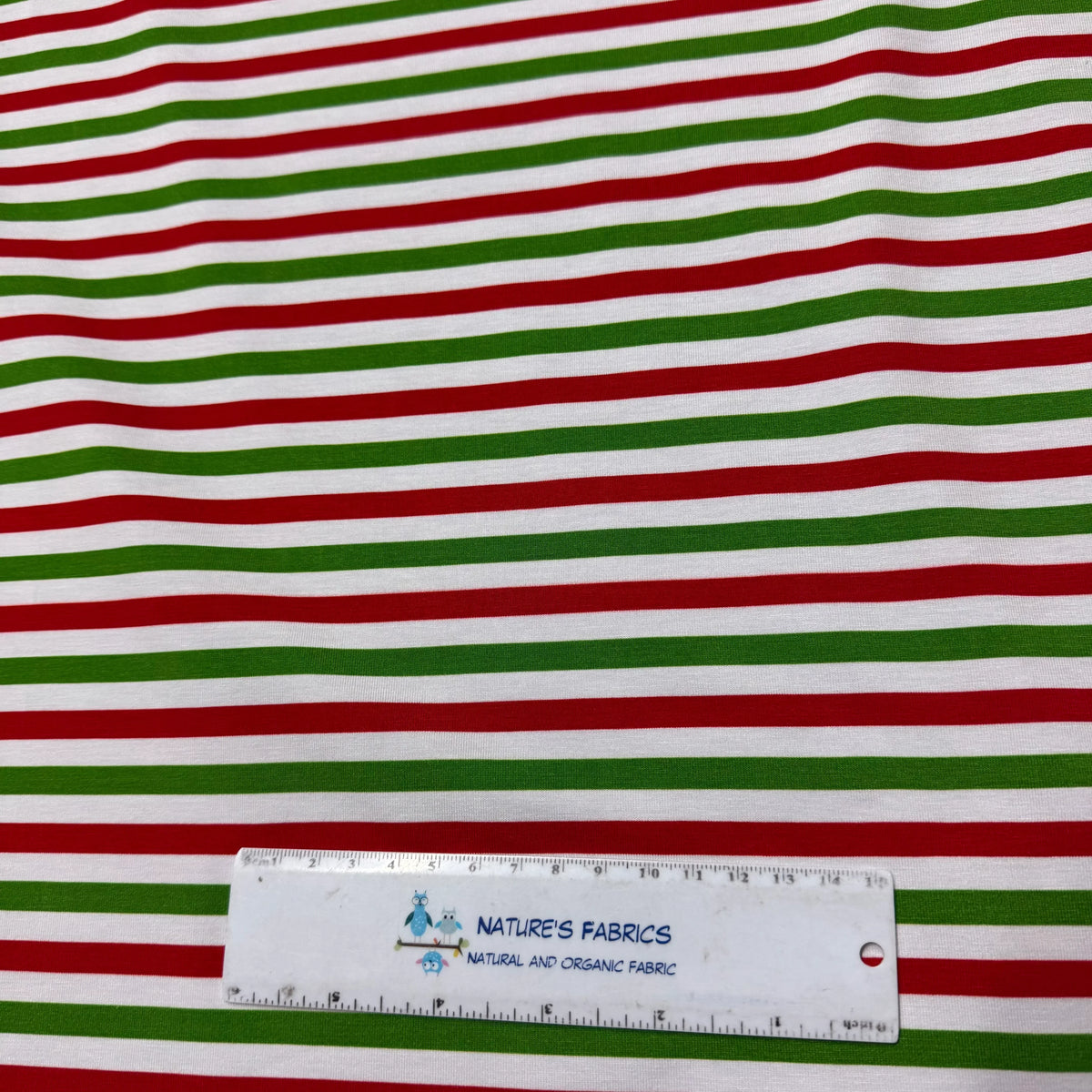 Red, green, and white striped organic cotton fabric by Nature's Fabrics with ruler for scale