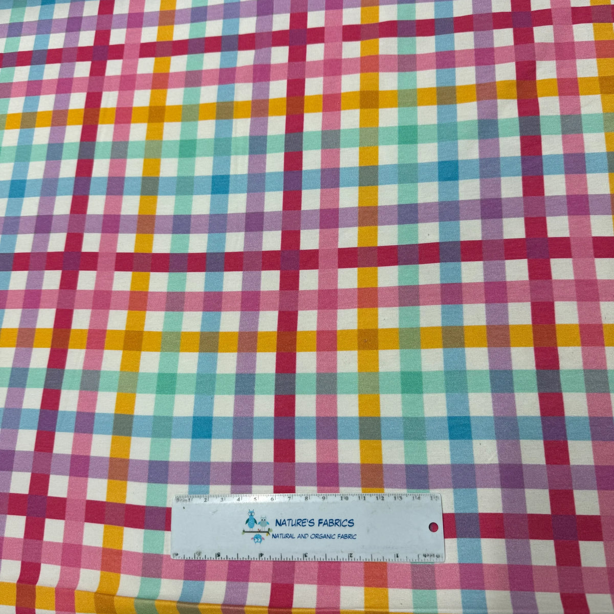 Colorful gingham fabric by Nature's Fabrics, featuring pink, blue, yellow, and green checks with a ruler for scale.