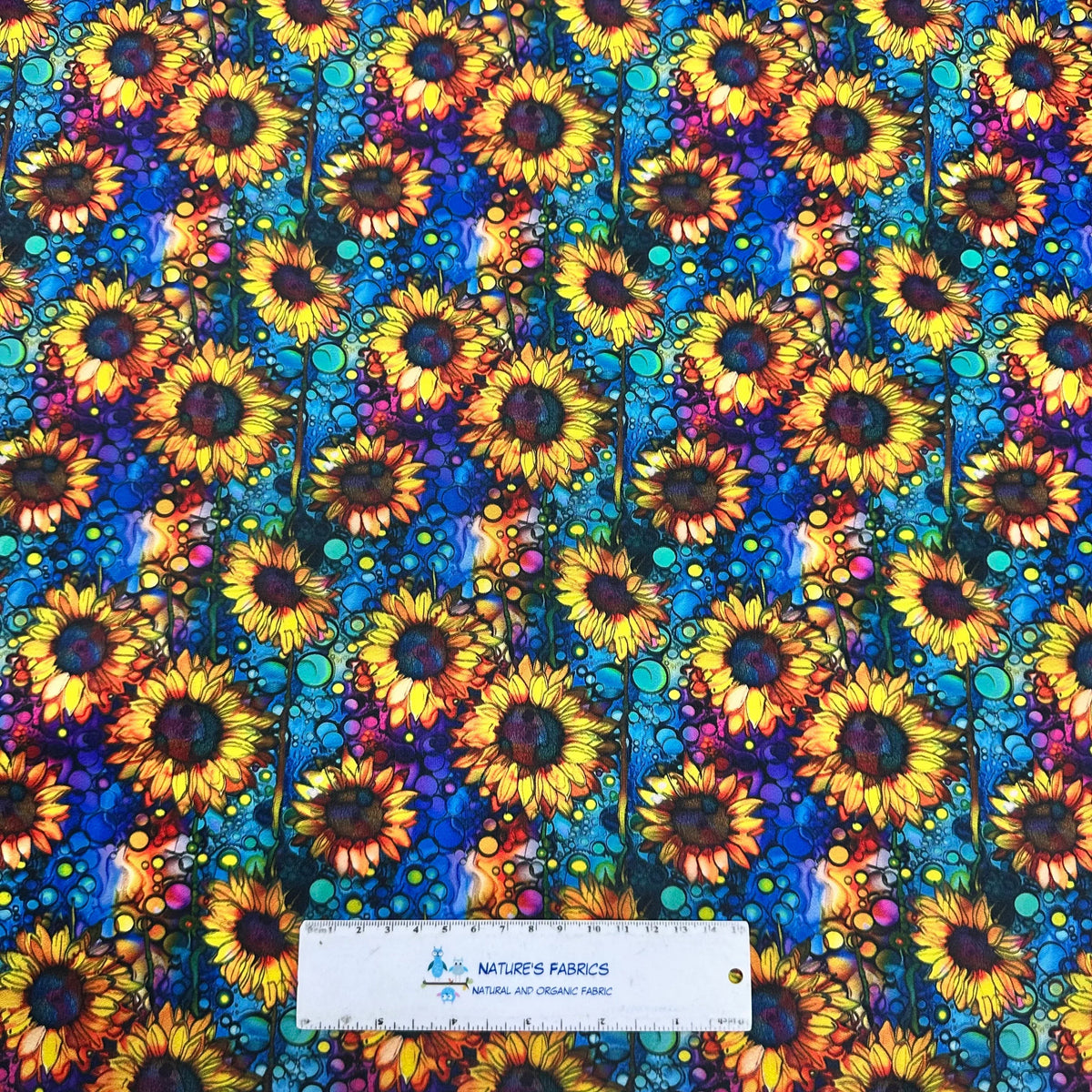 Vibrant sunflower print fabric by Nature's Fabrics, featuring bold yellow blooms on a colorful abstract background.