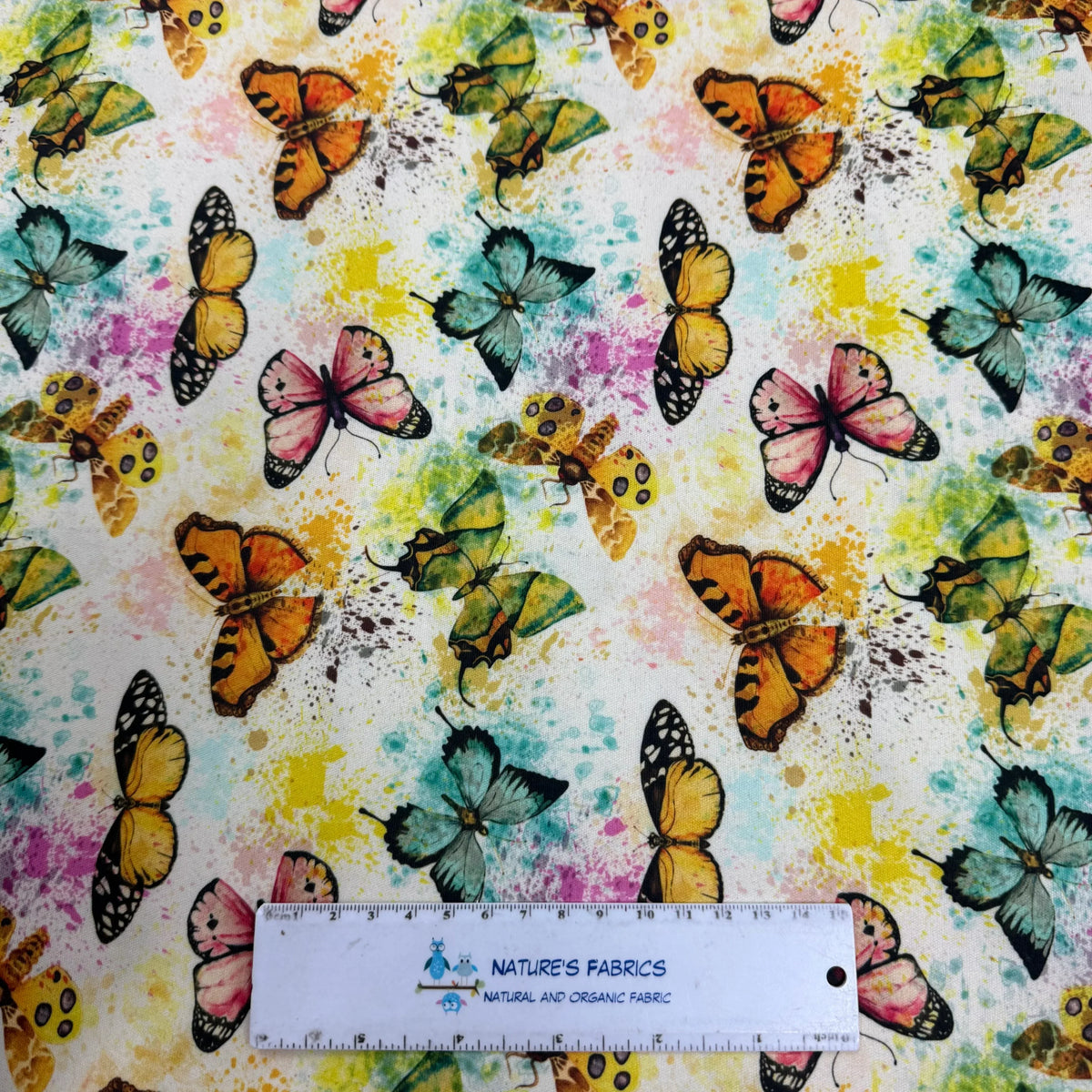 Colorful butterfly print fabric by Nature's Fabrics, featuring vibrant watercolor-style butterflies on natural organic cotton, ideal for quilting and crafts.