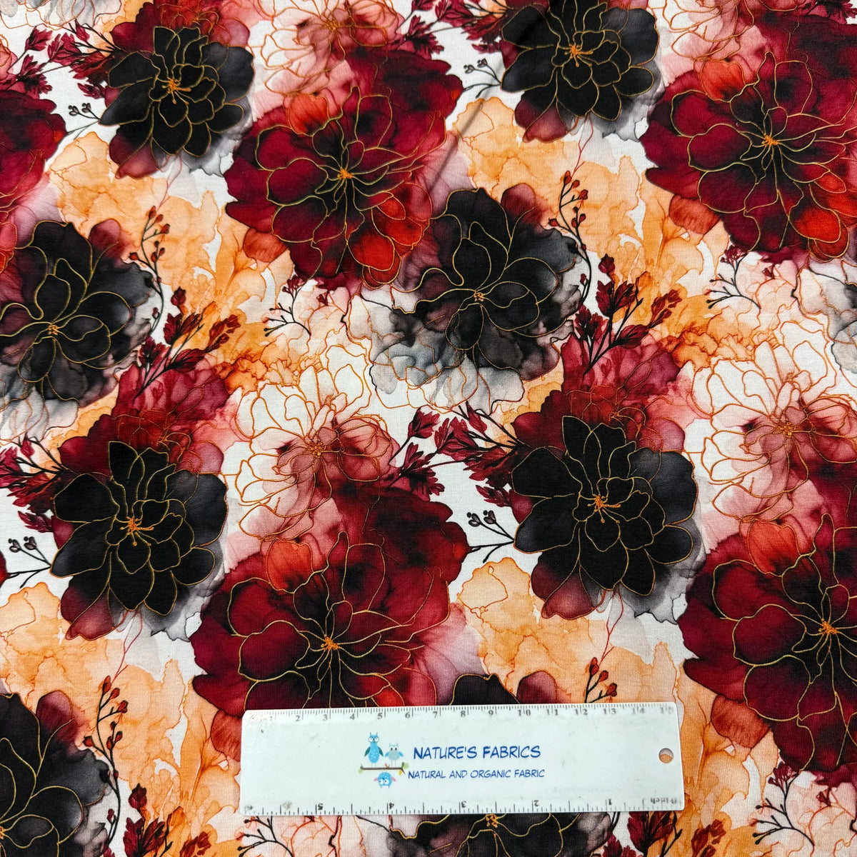 Nature's Fabrics floral print fabric with bold red, black, and orange watercolor flowers, gold outlines, and ruler for scale.