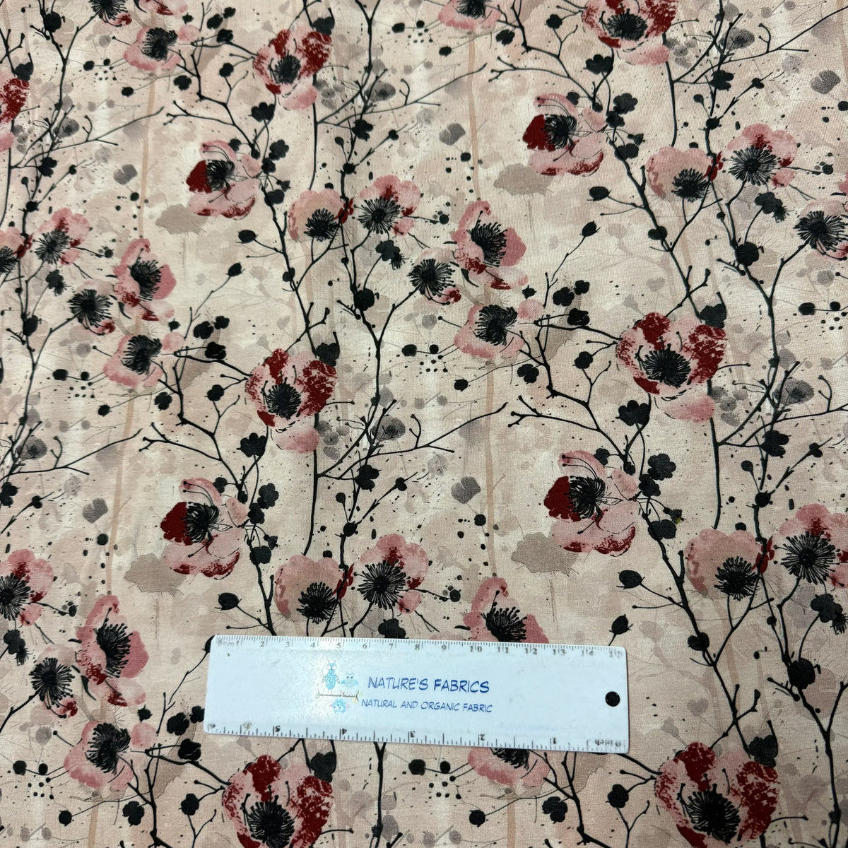 Nature's Fabrics floral print organic cotton fabric with pink and red blooms, black stems, and ruler for scale