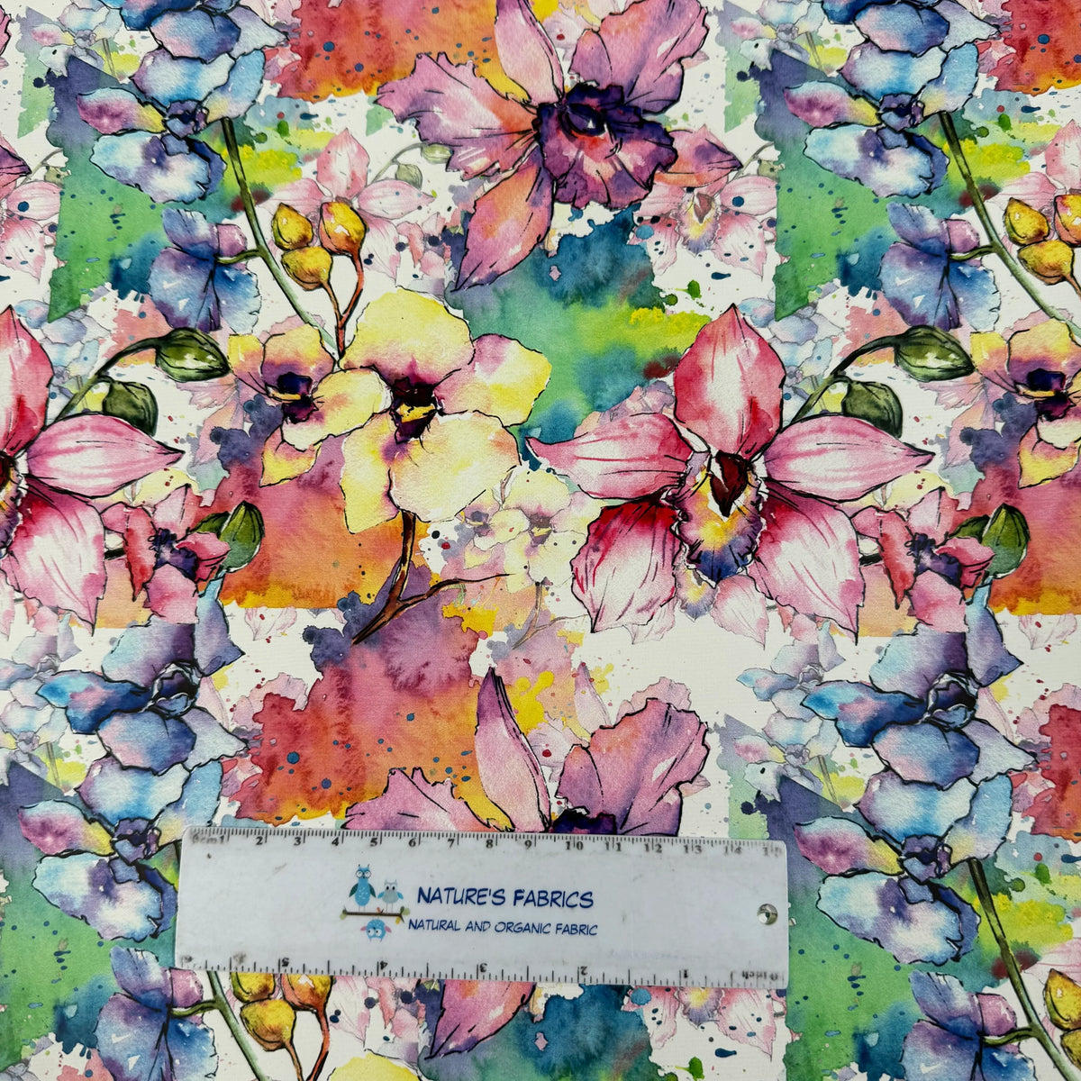 Vibrant watercolor floral print fabric by Nature's Fabrics, featuring colorful blossoms and organic cotton texture.