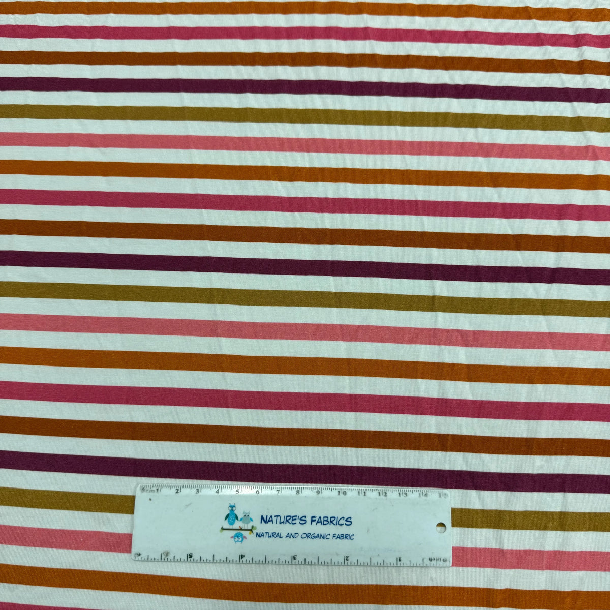 Nature's Fabrics multi-colored striped organic cotton fabric with a measuring ruler.