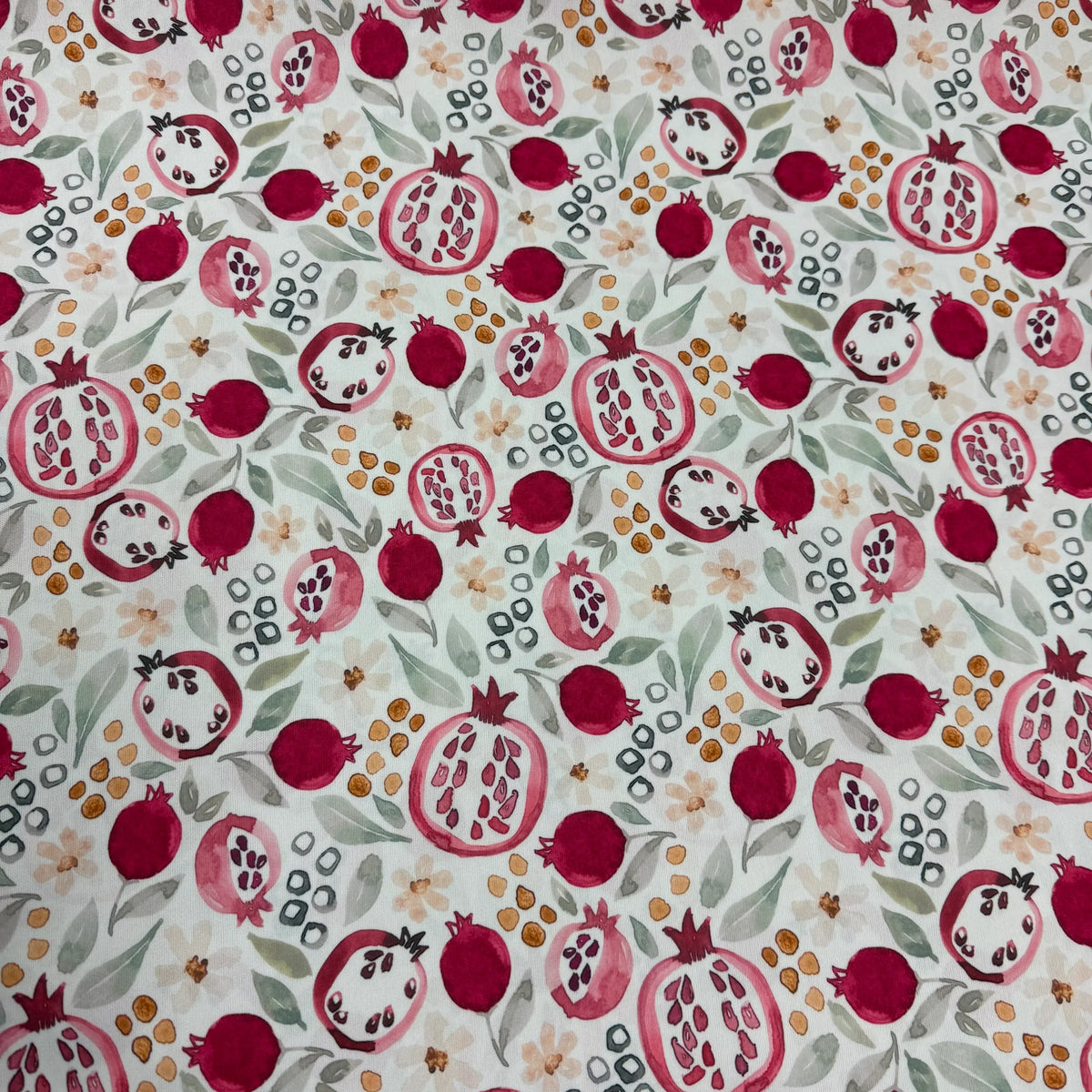 Pomegranate print fabric by Nature's Fabrics, featuring red fruit, green leaves, and floral accents on white background