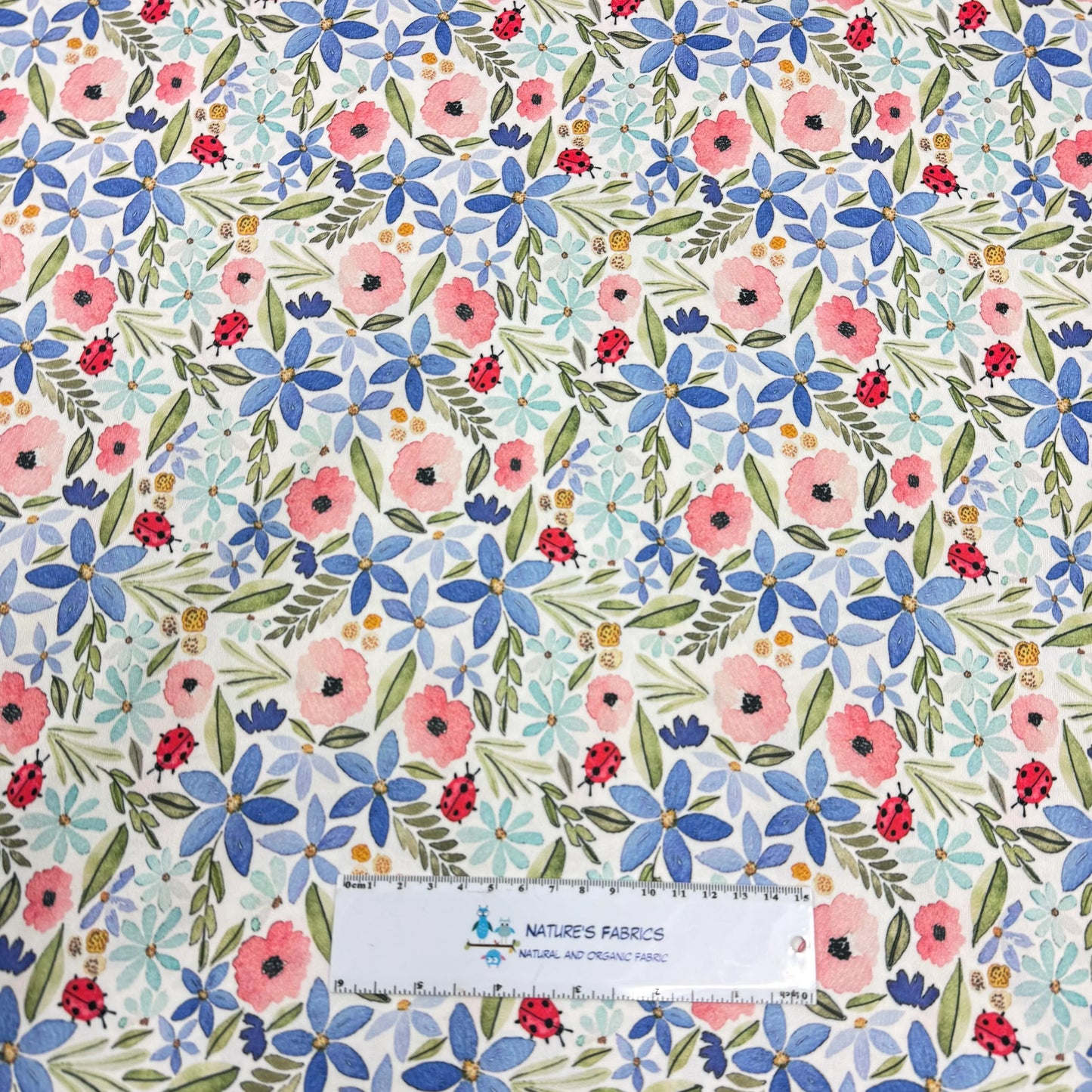 Nature's Fabrics floral print with blue and pink flowers, green leaves, and red ladybugs on white background
