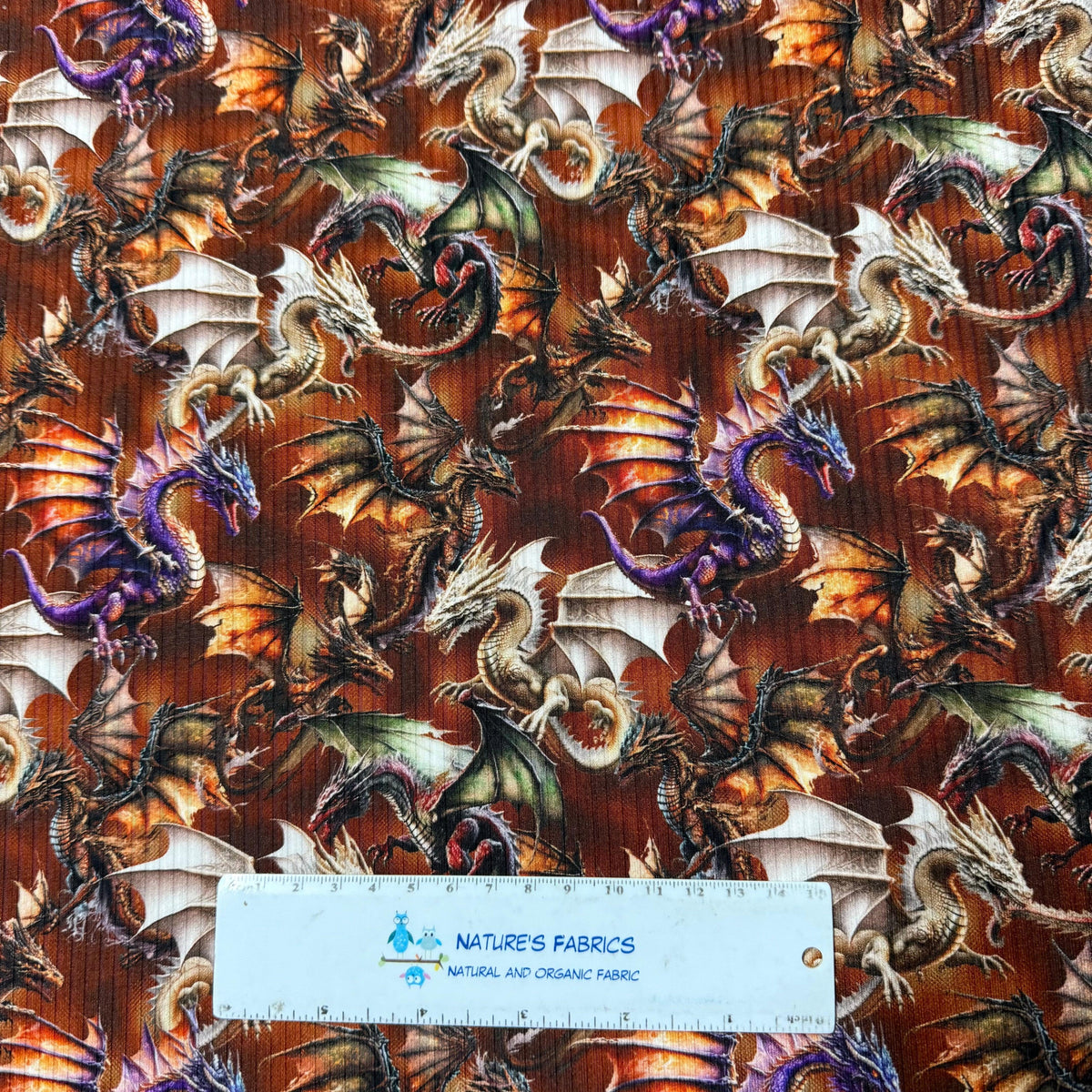 Dragon print fabric by Nature's Fabrics, featuring colorful mythical dragons on a rich brown background, perfect for fantasy-themed projects.
