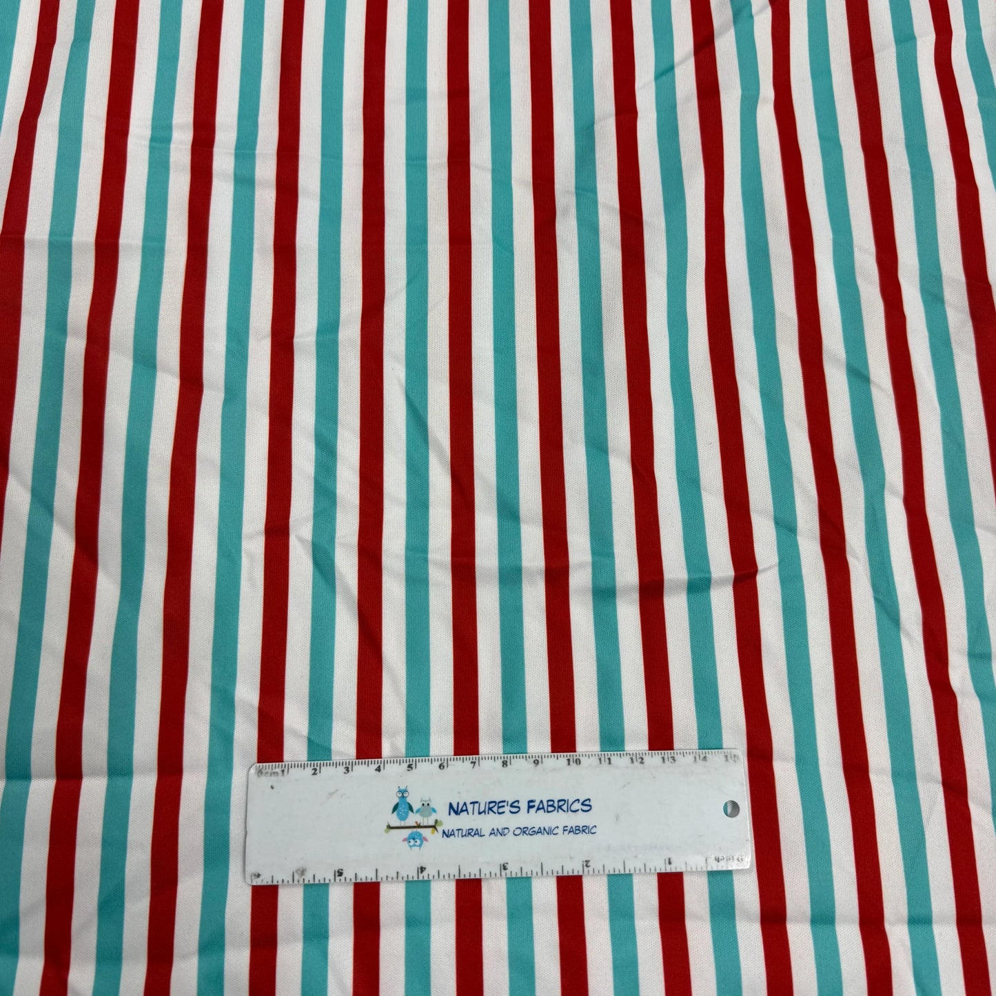 Red, teal, and white striped organic cotton fabric by Nature's Fabrics with ruler for scale