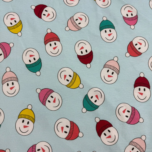 Snowman faces in colorful hats and scarves on light blue fabric by Nature's Fabrics