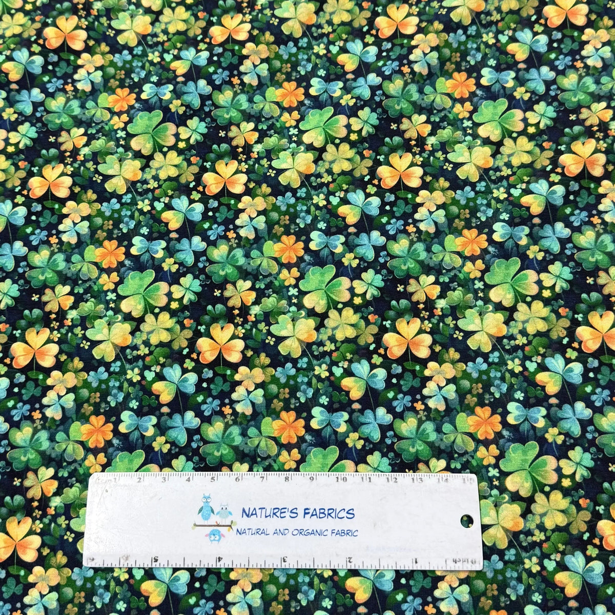 Nature's Fabrics shamrock print cotton fabric with green, blue, and orange clovers on dark background