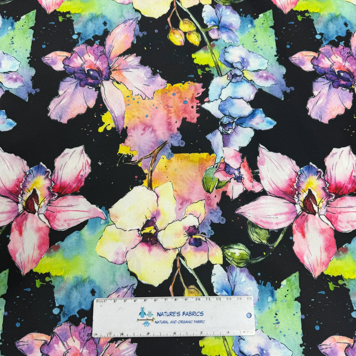 Nature's Fabrics watercolor floral print on black background, featuring vibrant pink, purple, and yellow blooms