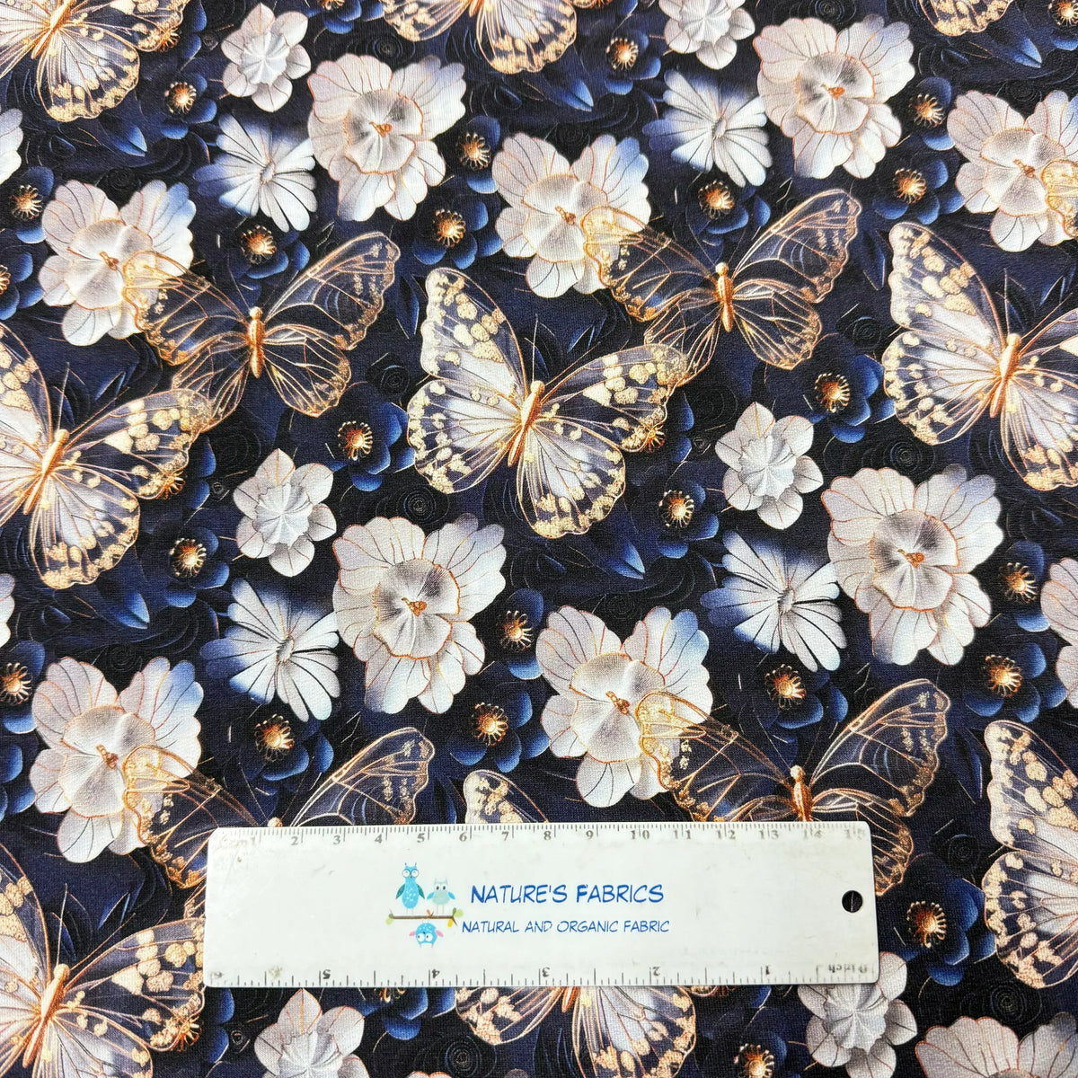 Nature's Fabrics butterfly and floral print fabric with ruler for scale, featuring white flowers and gold-accented butterflies on dark background