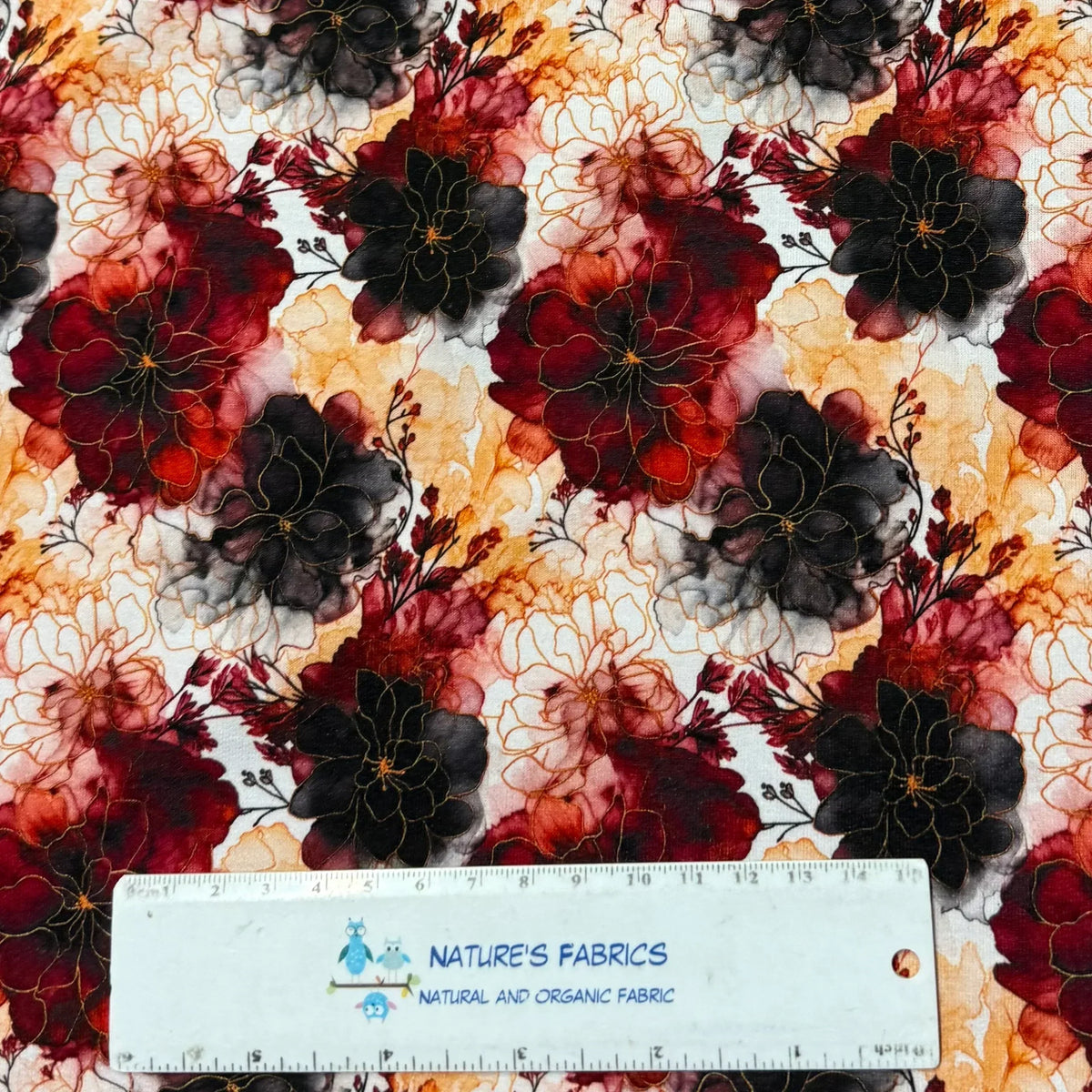 Nature's Fabrics floral print fabric with burgundy, black, and gold flowers on white background, ruler for scale