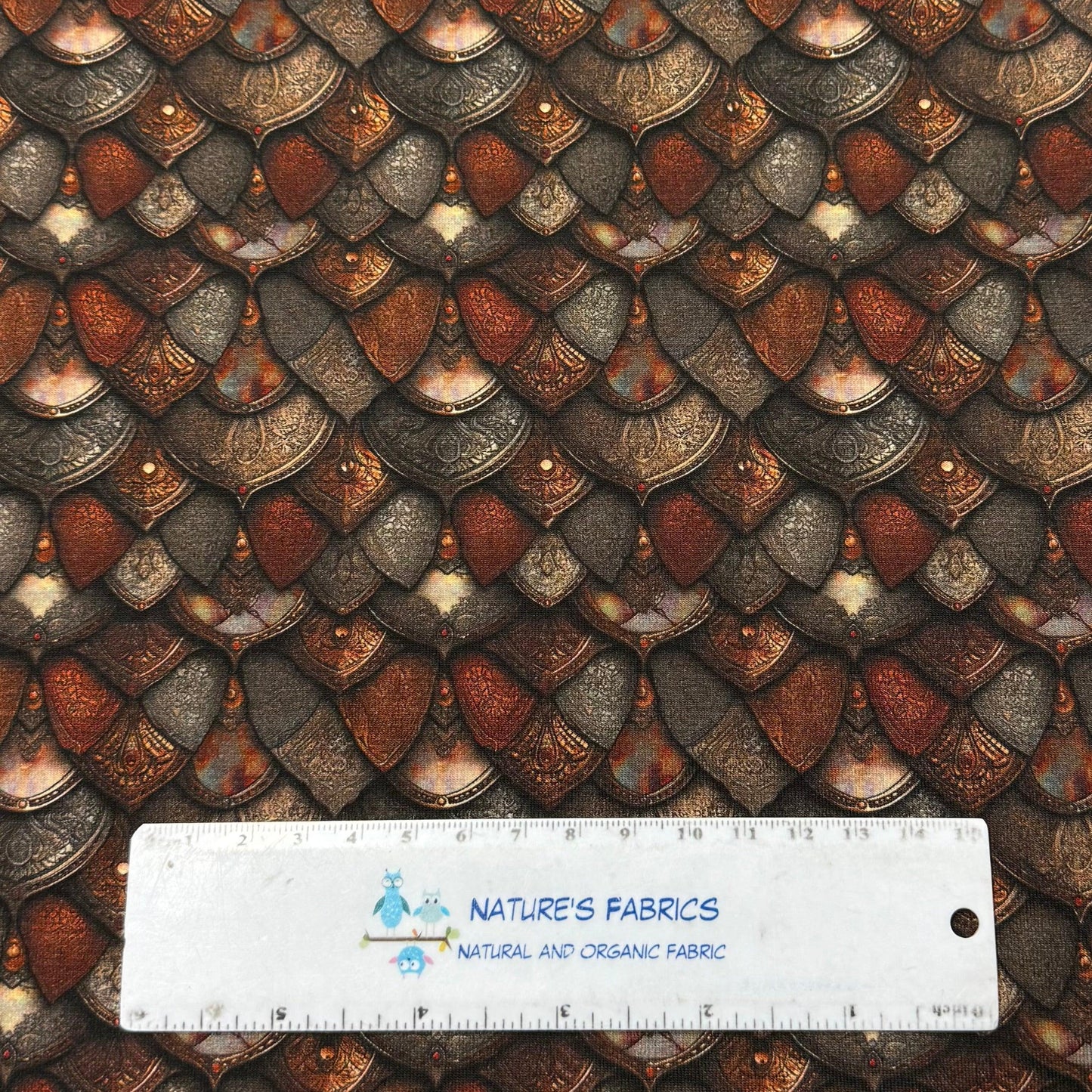 Dragon scale print fabric by Nature's Fabrics, featuring metallic bronze and copper scales with ruler for scale