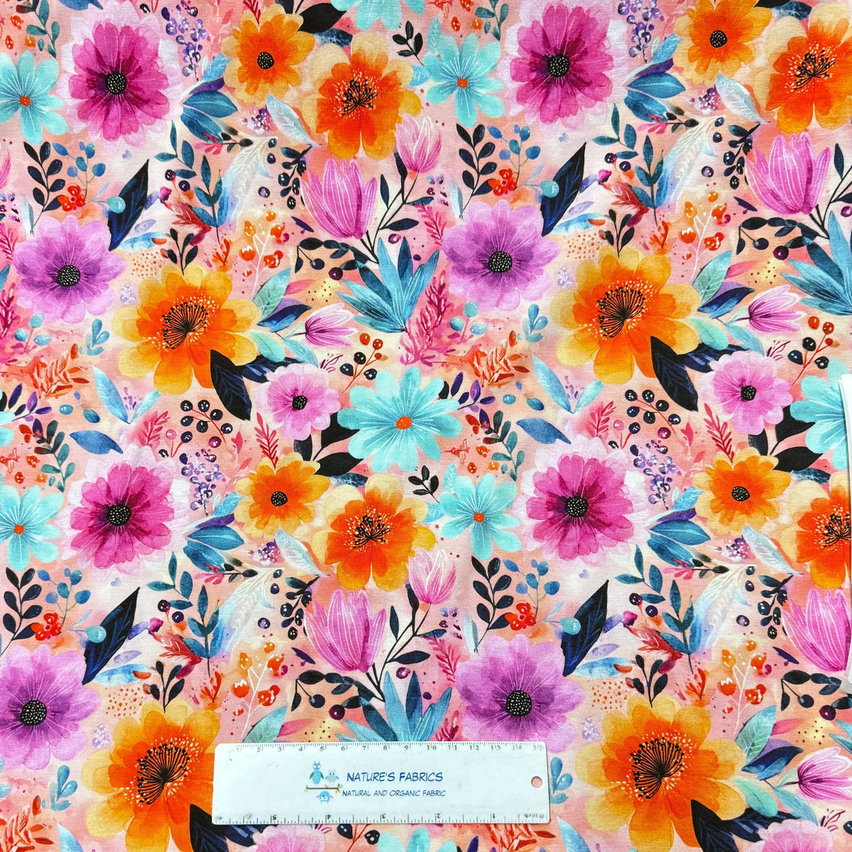 Vibrant floral print fabric by Nature's Fabrics, featuring pink, orange, and teal flowers on a soft background, ideal for sewing and crafts.