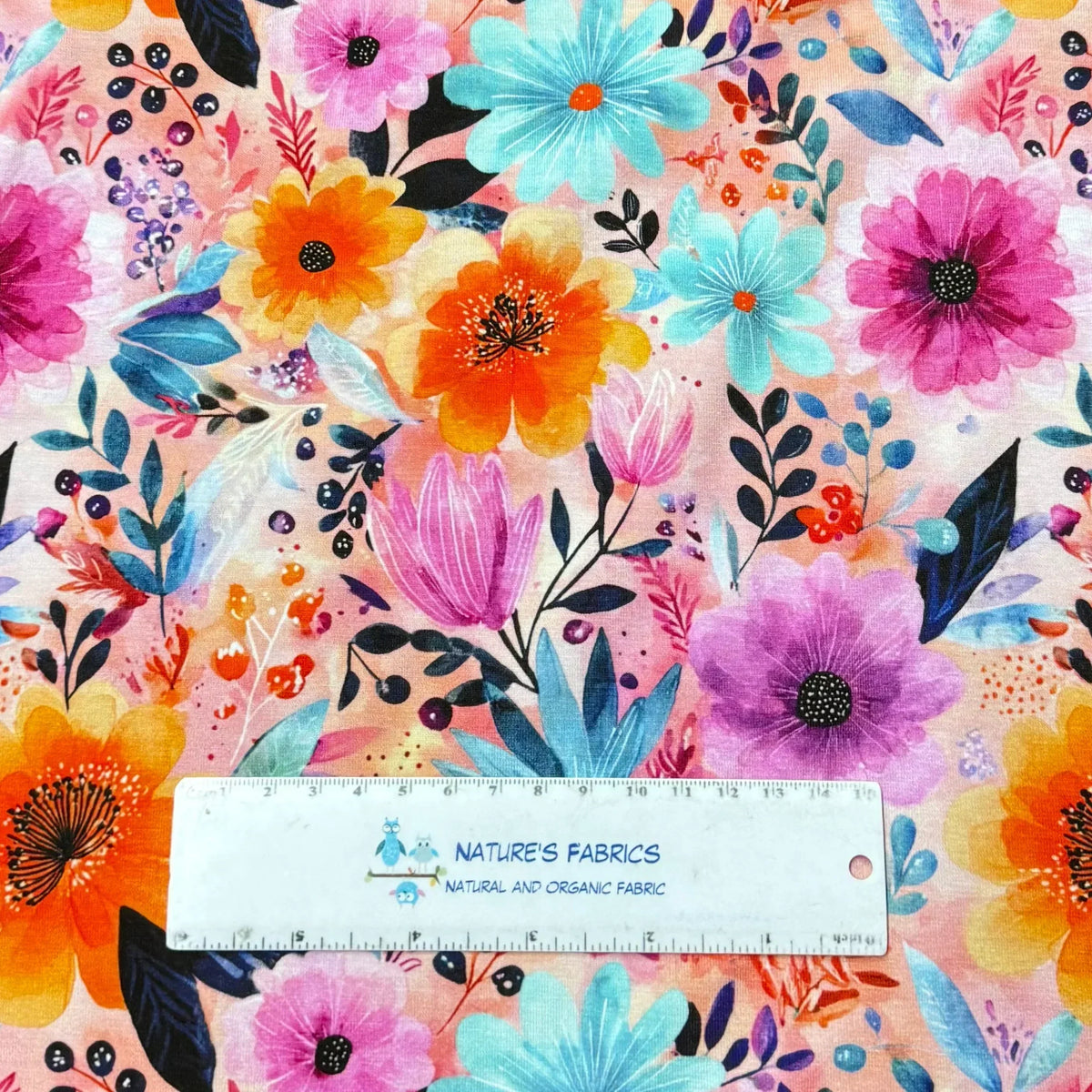 Vibrant floral print fabric by Nature's Fabrics, featuring colorful blooms and leaves on soft cotton, ideal for sewing projects.