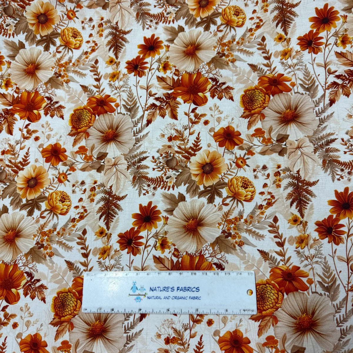 Nature's Fabrics autumn floral print fabric with orange, brown, and cream flowers, shown with ruler for scale
