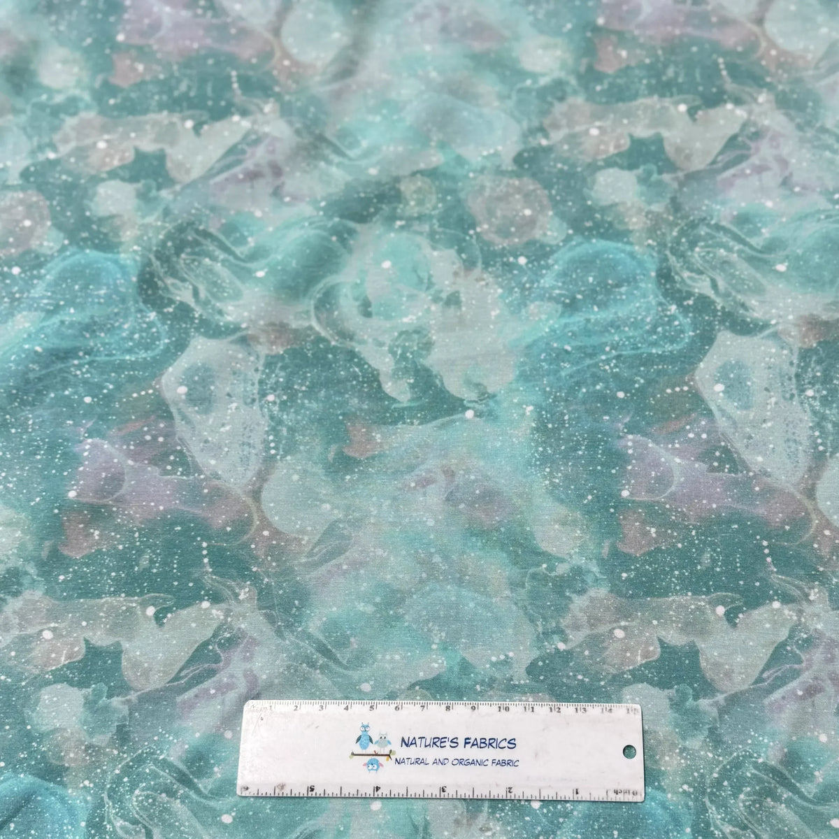 Nature's Fabrics teal and purple galactic marble print organic fabric with ruler for scale.