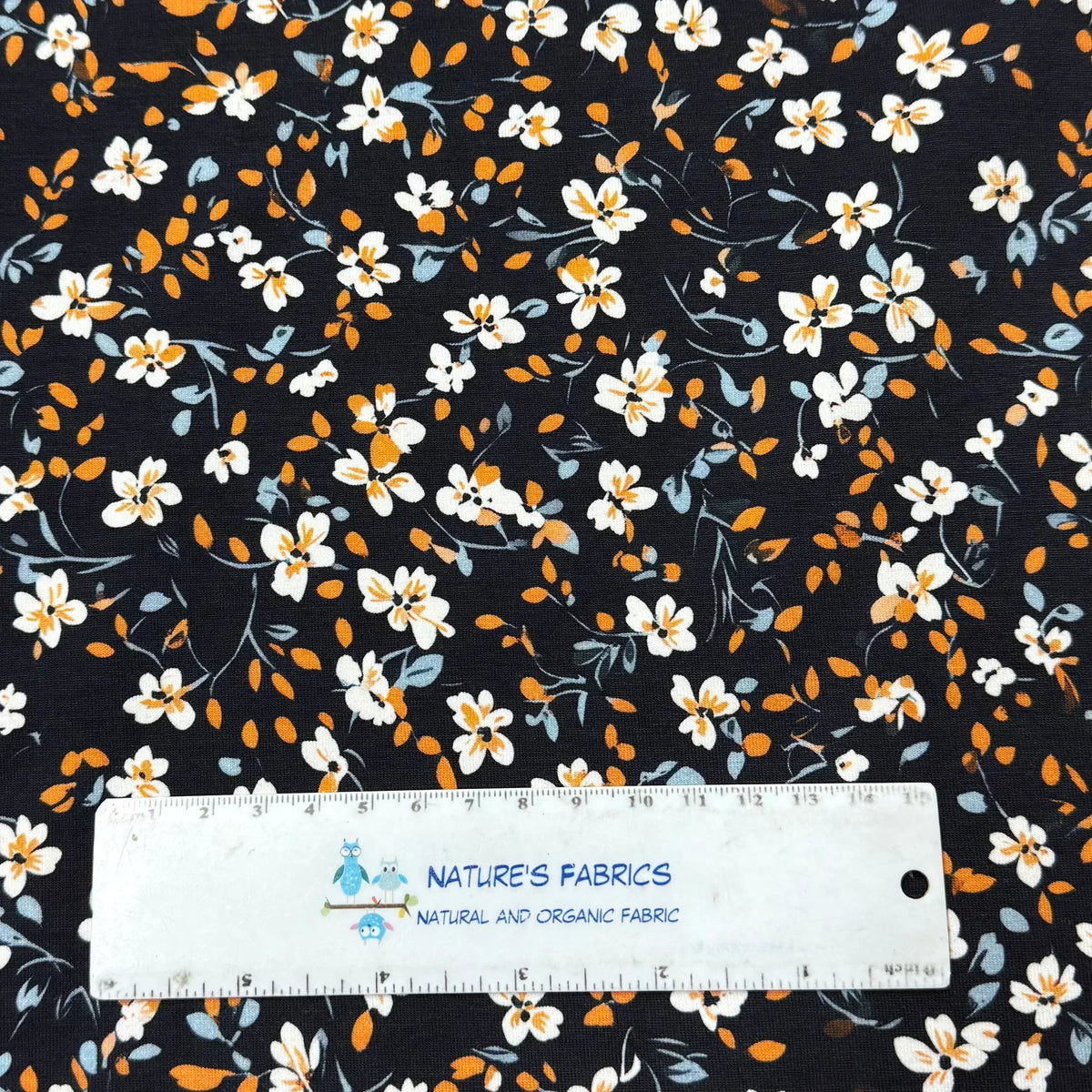 Nature's Fabrics floral print fabric with white and orange flowers on dark background, ruler for scale