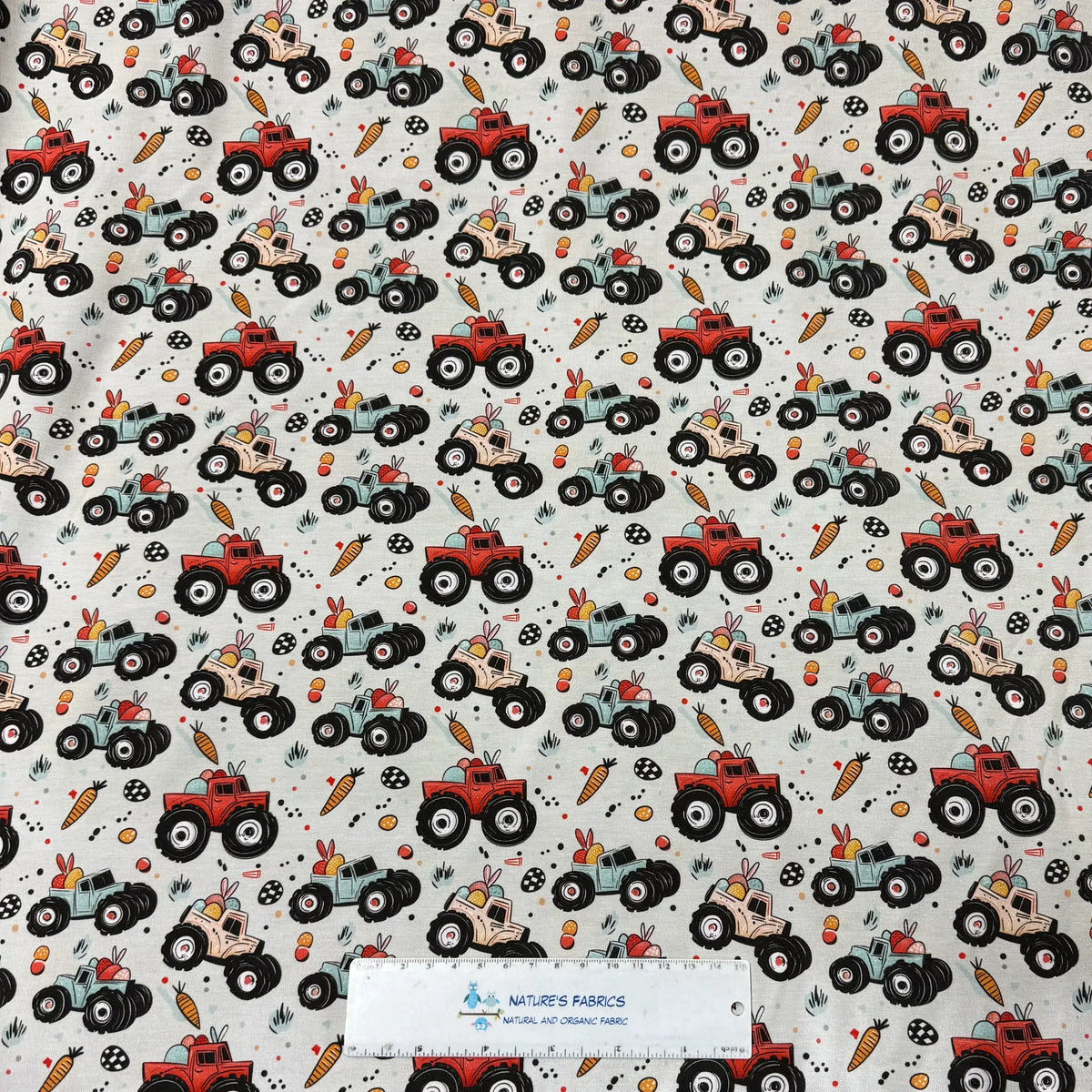 Nature's Fabrics Easter monster truck print fabric with colorful trucks, carrots, and eggs on light background