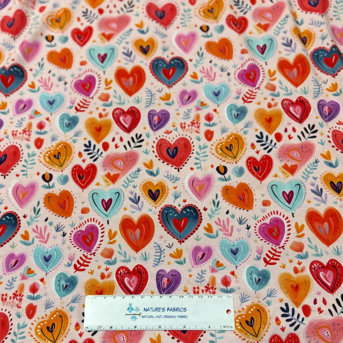 Colorful heart pattern fabric by Nature's Fabrics, featuring vibrant hearts and leaves on natural organic cotton.
