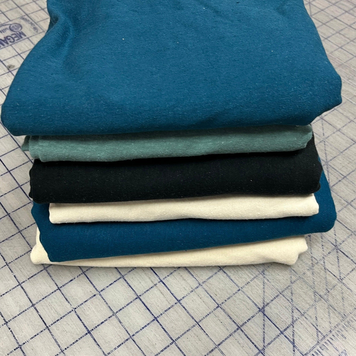 Stack of Nature's Fabrics premium natural fabric in blue, teal, black, and white colors.