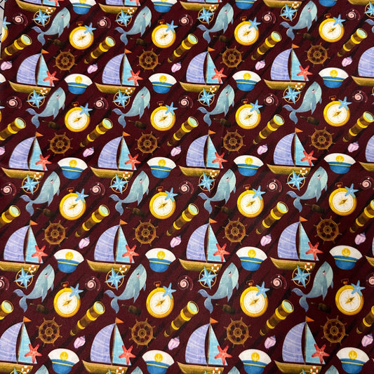 Nature's Fabrics maroon cotton fabric with nautical print of sailboats, whales, and compasses.