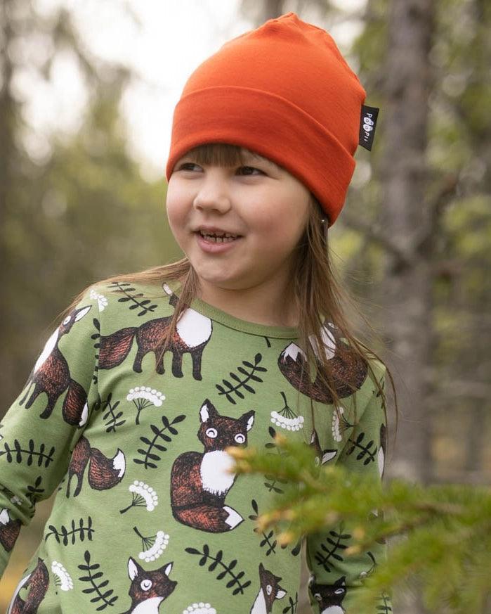 Young girl wearing a Nature's Fabrics green fox print shirt and orange beanie outdoors.