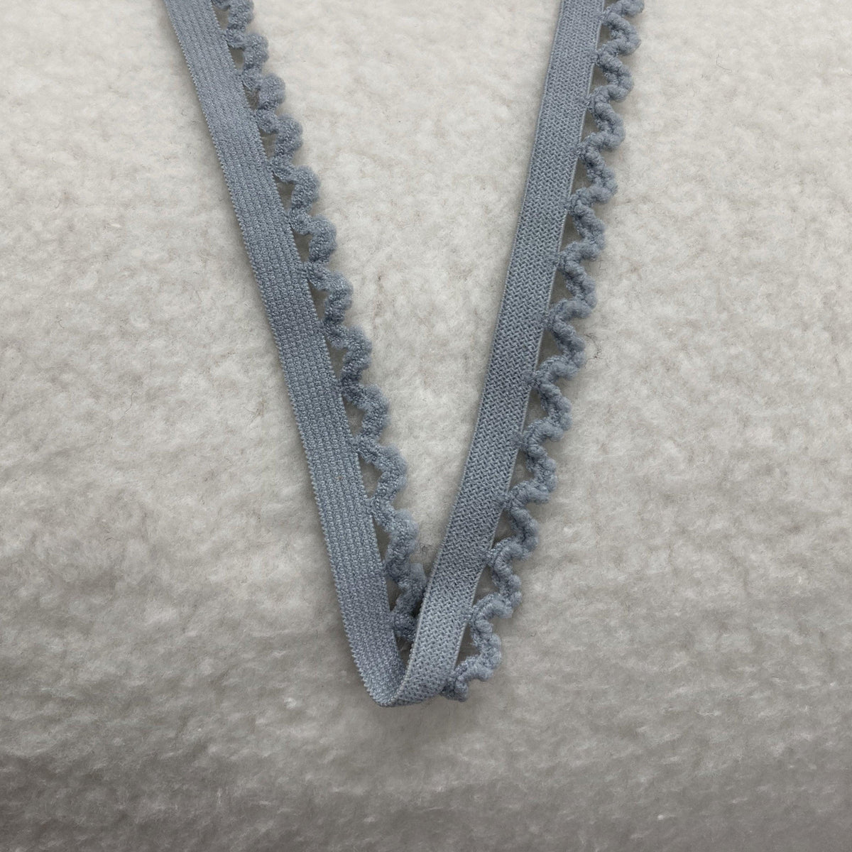 Nature's Fabrics light gray elastic trim with a scalloped edge on a textured white surface