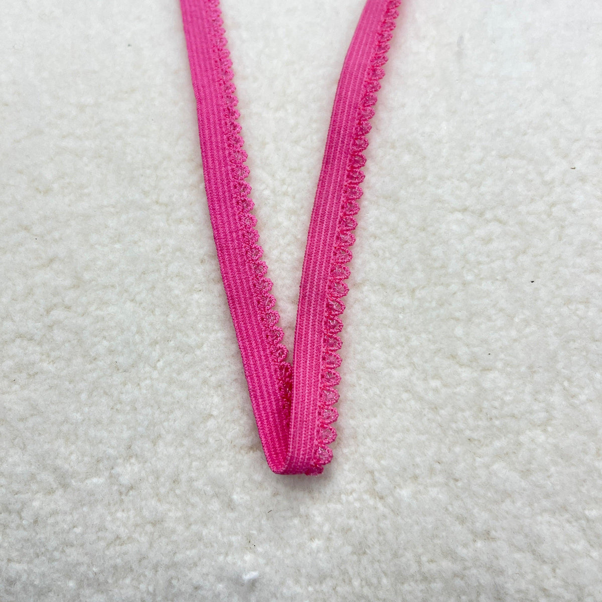 Hot pink scalloped lace trim ribbon from Nature's Fabrics on a white textured background