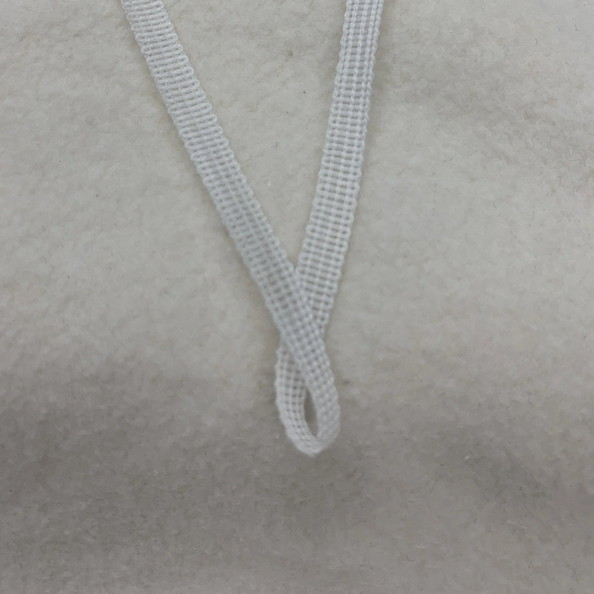 Close-up of a white elastic strap from Nature's Fabrics on a textured white background.