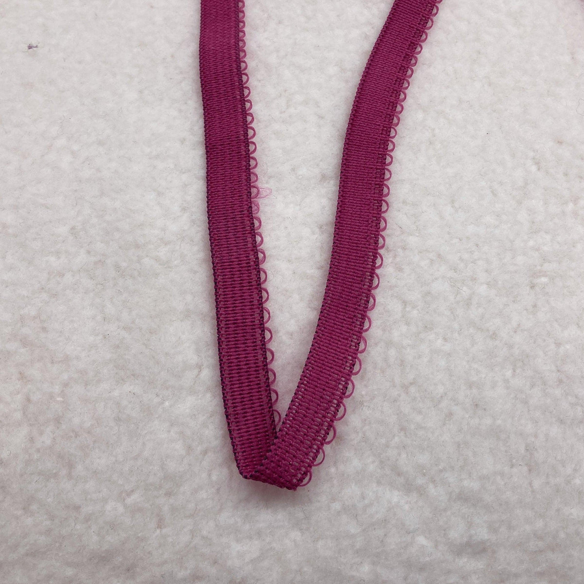Nature's Fabrics magenta pink scalloped edge elastic ribbon on a white textured background