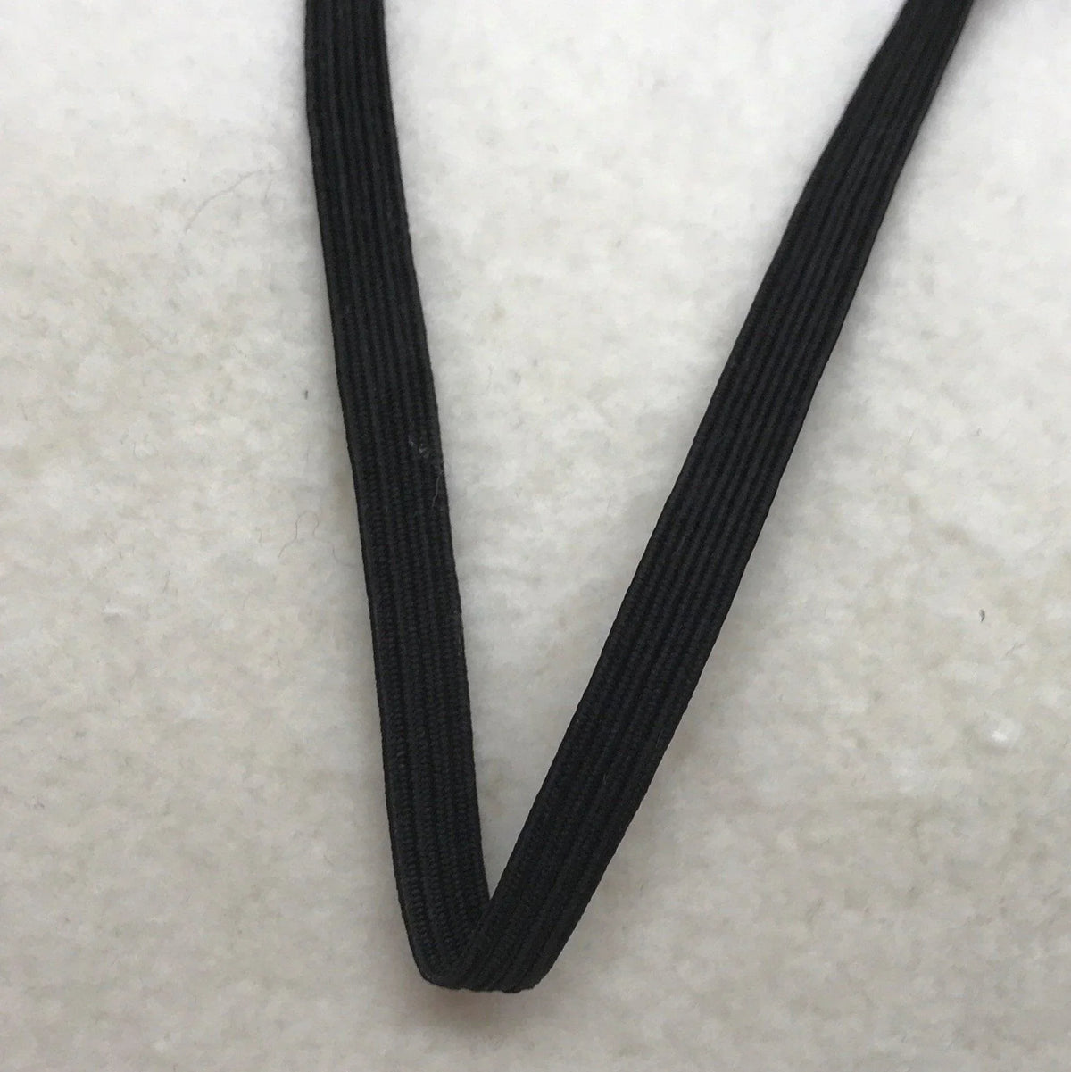Close-up of black Nature's Fabrics elastic cord on a white textured surface.