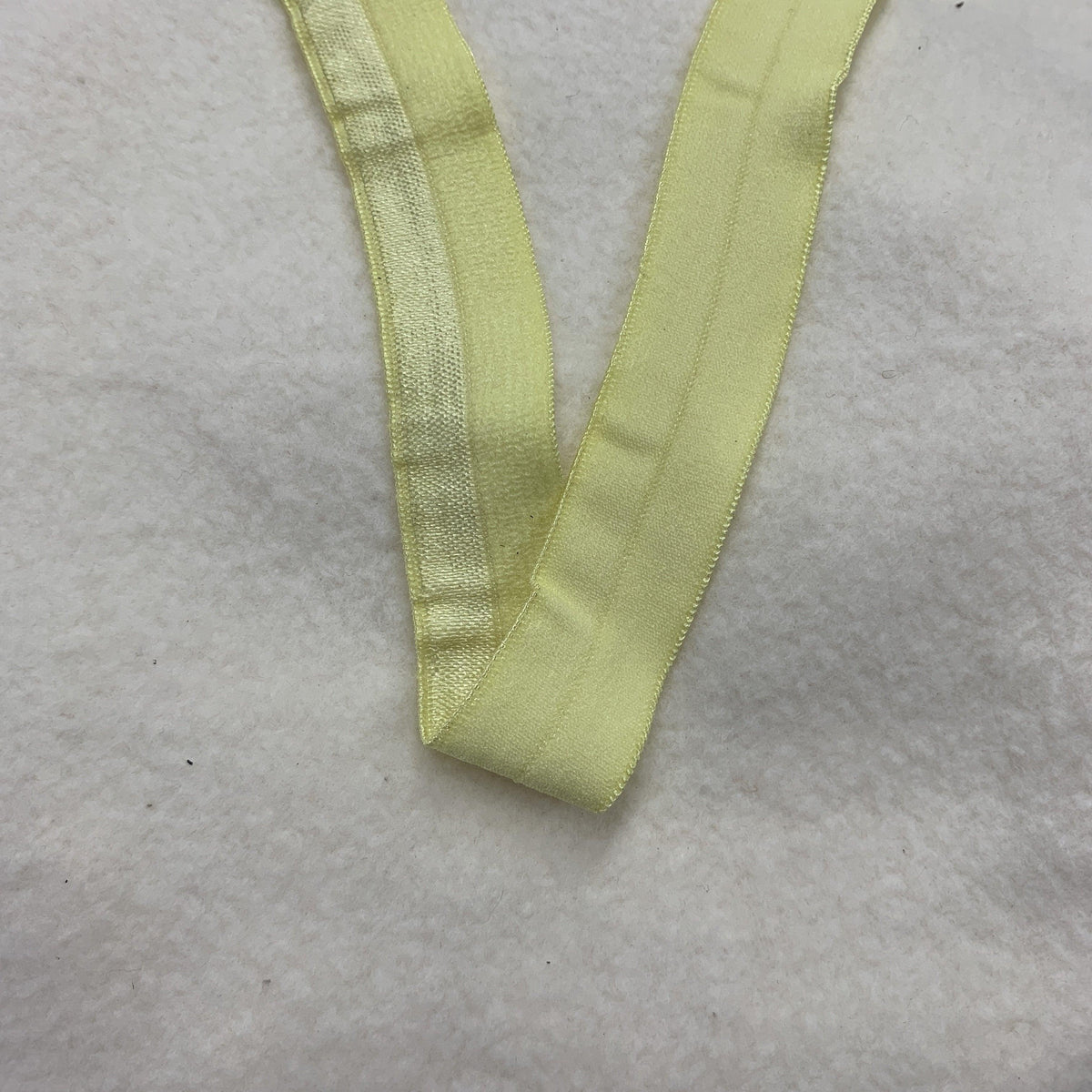 Pale yellow Nature's Fabrics ribbon on a white textured background.